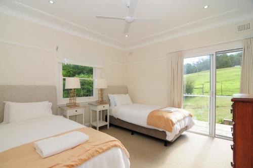 a white bedroom with two beds and a window at Nellsville Cottage Kangaroo Valley in Upper Kangaroo River