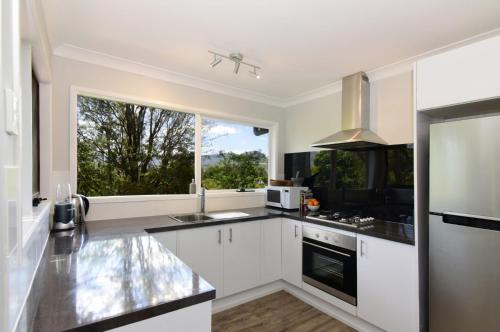 a kitchen with white cabinets and a large window at Treetops - Three bedroom home with great views, in the village! in Kangaroo Valley