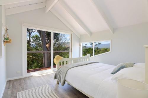 a white bedroom with a bed and two windows at Treetops - Three bedroom home with great views, in the village! in Kangaroo Valley