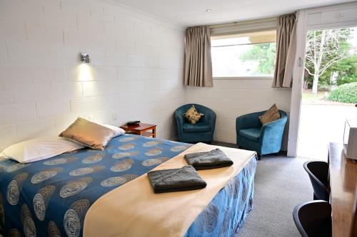 a bedroom with a bed and two blue chairs at Byer Fountain Motor Inn in Holbrook