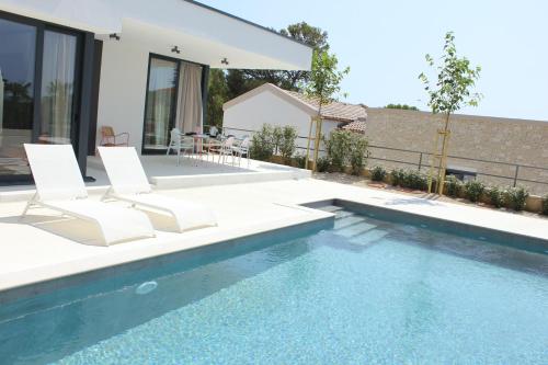 a swimming pool with two chairs and a house at Villa Sunny Garden in Barbat na Rabu