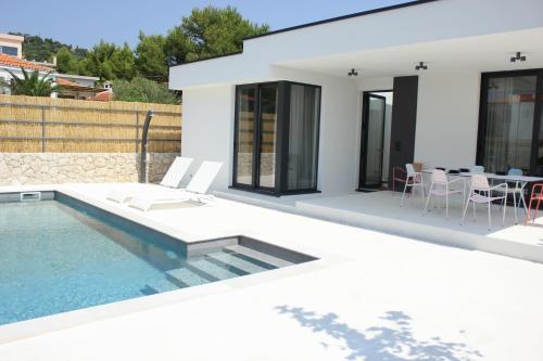 a white house with a swimming pool and a table at Villa Sunny Garden in Barbat na Rabu