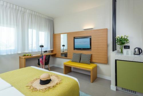 um quarto com uma cama, uma televisão e uma cadeira amarela em Prima Galil Tiberias Hotel em Tiberias