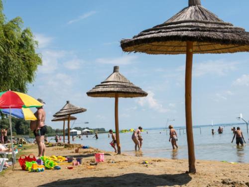 een groep mensen op een strand met parasols bij Napocska Panzió in Vonyarcvashegy