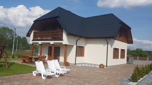 une maison avec un toit noir et des chaises blanches dans l'établissement Apartamenty Białowieża, à Białowieża