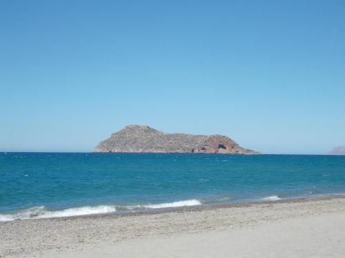 a beach with a rocky island in the ocean at Lissos Beach in Plataniás