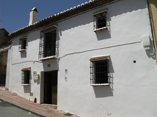 a white building with barred windows on a street at La Casa de Corruco in Casabermeja