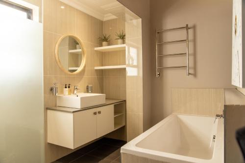 a bathroom with a sink and a tub and a mirror at 2 On Lismore Guesthouse in Tokai