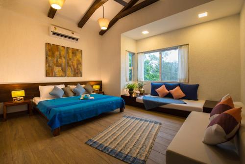 a bedroom with a blue bed and a couch and a window at EL Lodge by StayVista - Pool, lawn, and a charming gazebo for your perfect getaway in Lonavala