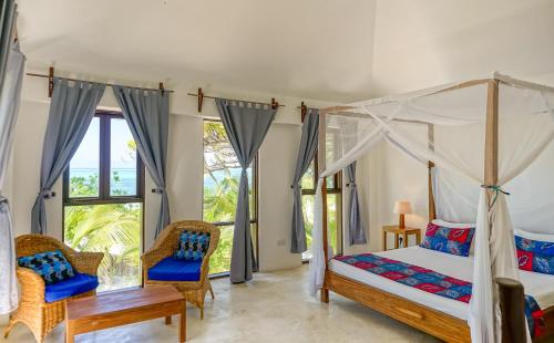a bedroom with a canopy bed and two chairs at Indigo Beach Zanzibar in Bwejuu