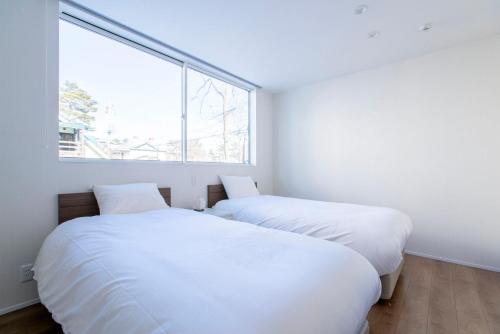 two beds in a white room with a window at Hakuba White Fox Chalet in Hakuba