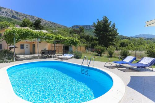 a swimming pool with two blue chairs and a house at Holiday Home Rupotina with a large yard, pool and a beautiful view in Solin