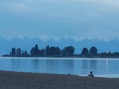 a person sitting on the shore of a lake at Boomerang Guest house in Cholpon-Ata
