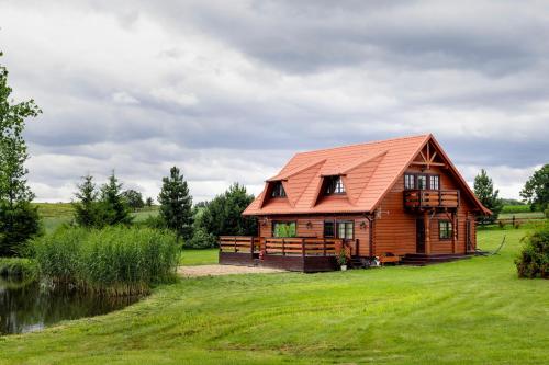 a wooden cabin with a red roof on a grass field at CHATY ZA WSIĄ in Mrągowo