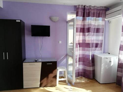 a room with a purple wall with a desk and a tv at Къща за гости "Пердика" in Obzor