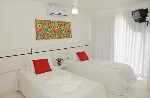 two white beds in a white room with red pillows at Residencial Mont Sião - Tonziro in Porto Seguro