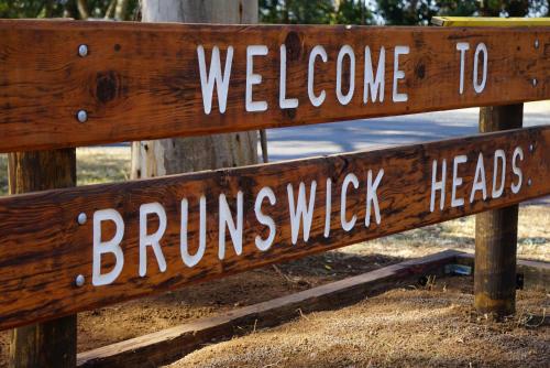 een houten bord waarop staat: welkom bij brunswick heads en headsheads bij Brunswick Heads Treetop Studio in Brunswick Heads