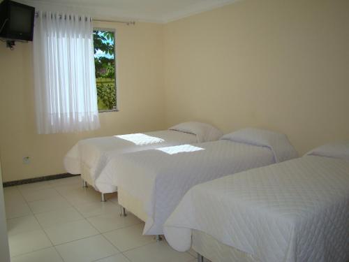 a room with three beds and a television and a window at Hotel Absolar in Alagoinhas