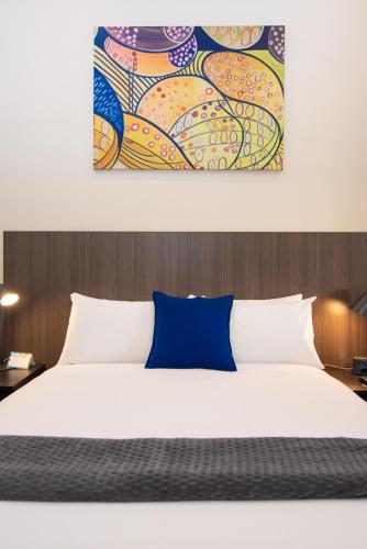 a bedroom with a white bed and a painting on the wall at The Mile End Hotel in Adelaide