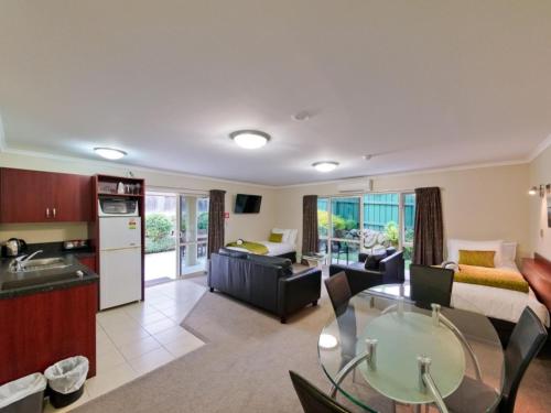 cocina y sala de estar con mesa de cristal en una habitación en ASURE Avenue Motor Lodge, en Timaru