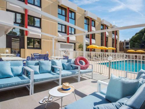 une terrasse avec des canapés bleus et une piscine dans l'établissement ibis Styles Nice Cap 3000 Aéroport, à Saint-Laurent-du-Var