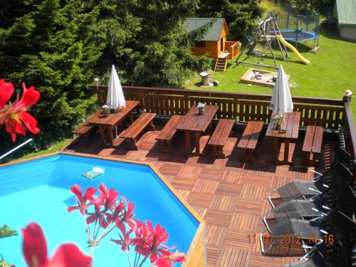 una piscina con mesas y sillas de madera y un parque infantil en Pension Holubec en Benecko