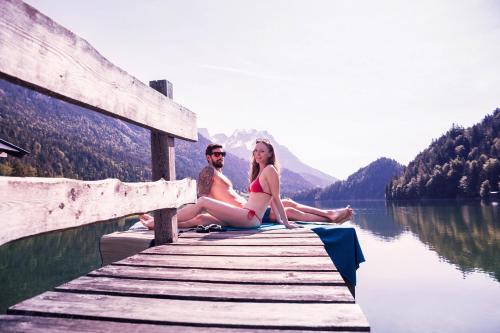 a man and a woman sitting on a dock on a lake at Tirol Lodge in Ellmau