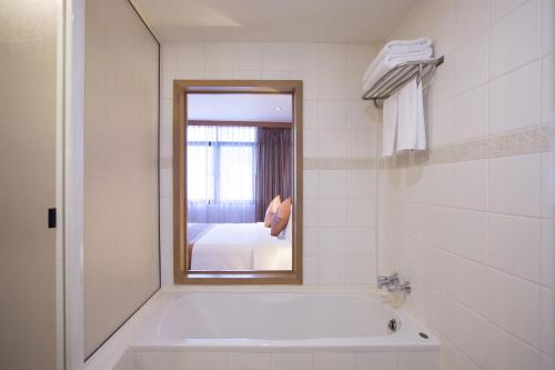 a bathroom with a tub and a mirror and a bed at The Tarntawan Hotel Surawong Bangkok in Bangkok