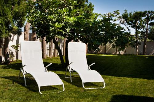 two white chairs sitting in the grass next to a tree at B&B 7Cento Ulivi in Valderice