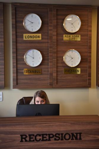 a woman sitting at a desk in an office with clocks on the wall at Prior Hotel in Prizren