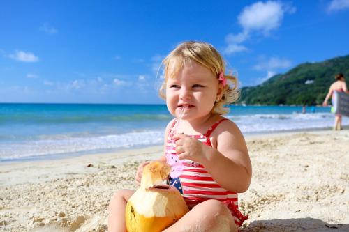 a little girl sitting on the beach with a straw at Savoy Seychelles Resort & Spa in Beau Vallon