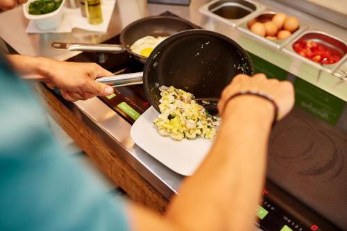 a person cooking food in a pan on a stove at Explorer Hotel Bad Kleinkirchheim in Bad Kleinkirchheim