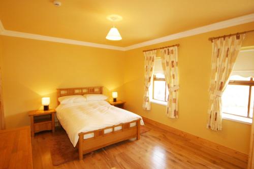 a yellow bedroom with a bed and two windows at Yewwood Cottage in Newry