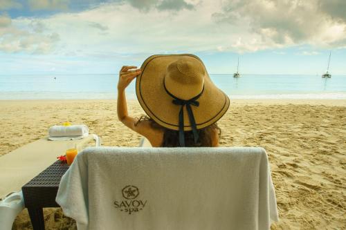 a person sitting on the beach wearing a hat at Savoy Seychelles Resort & Spa in Beau Vallon