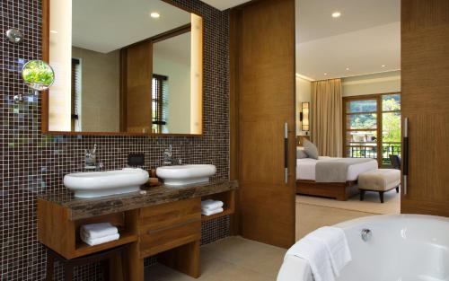 a bathroom with two sinks and a tub and a bedroom at Savoy Seychelles Resort & Spa in Beau Vallon