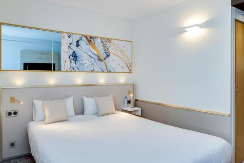 um quarto com uma cama branca e um espelho em Brit Hotel Orléans St Jean de Braye - L'Antarès em Saint-Jean-de-Braye