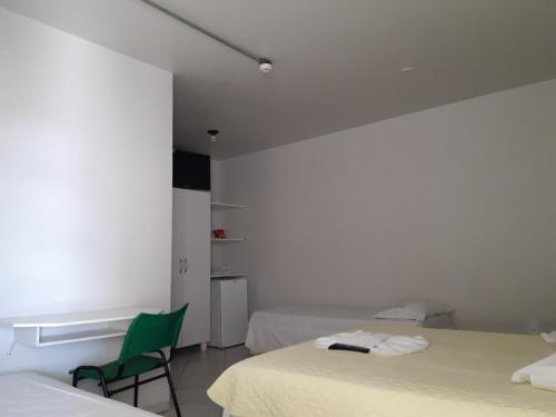 een witte kamer met 2 bedden en een groene stoel bij Hotel Master in Primavera do Leste