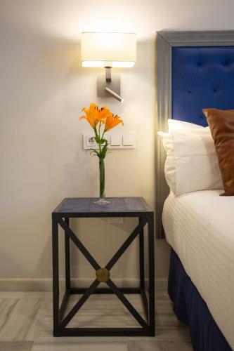 a vase of orange flowers on a table next to a bed at Plazuela del Carbón Suites in Cádiz
