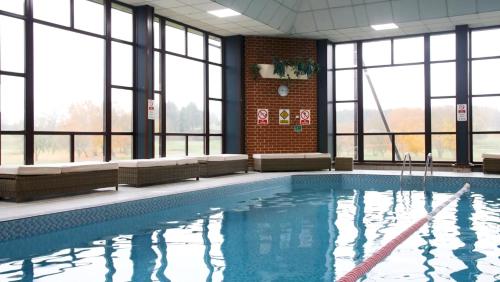 een zwembad in een gebouw met ramen bij Barnham Broom Hotel, Golf & Spa in Norwich