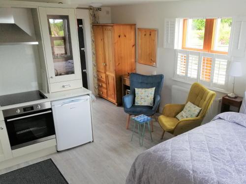 a bedroom with a bed and two chairs and a kitchen at BallyCairn Self Catering Studio in Larne