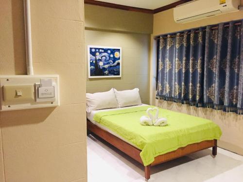 a bedroom with a bed with a green blanket and two rabbits on it at Nett Hotel in Lop Buri