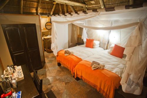 a bedroom with a canopy bed with orange pillows at Omarunga Epupa-Falls Camp in Opuwo