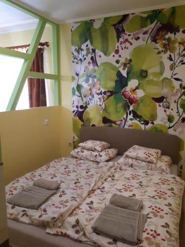 1 dormitorio con cama con almohadas y pared de flores en Rozmaring Apartmanok, en Gyula