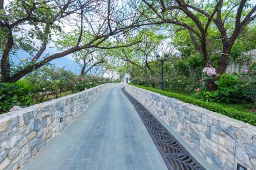 a walkway in a park with trees and a stone wall at Silk Path Grand Sapa Resort & Spa in Sa Pa