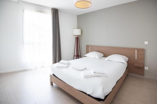 a white bedroom with a large bed with white sheets at Zenitude Hôtel-Résidences Narbonne Centre in Narbonne