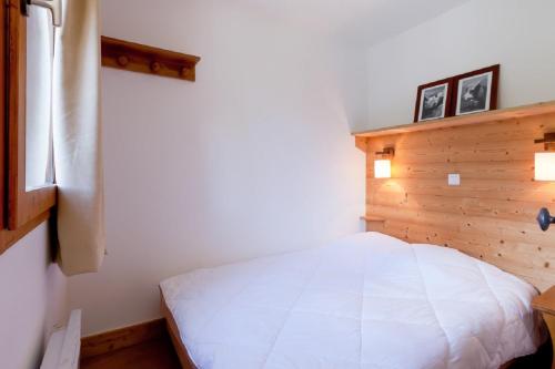 a bedroom with a white bed with a wooden wall at Residence Les Sentiers du Tueda - maeva Home in Méribel
