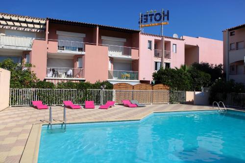 a swimming pool with pink chairs and a building at Hotel Les Grenadines in Cap d'Agde