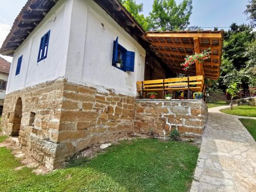 a stone house with blue windows and a stone wall at Stara etno kuća Radonjić in Guča