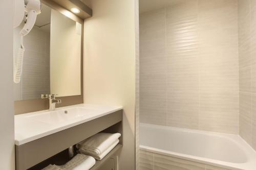 La salle de bains blanche est pourvue d'un lavabo et d'une baignoire. dans l'établissement Résidence Prestige Odalys Les Canissons, à Cavalaire-sur-Mer