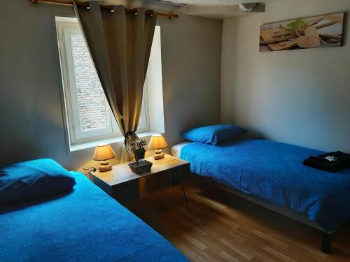 - 2 lits dans une chambre avec des draps bleus et une fenêtre dans l'établissement Les 3 Cailloux Bar Restaurant, à Gurgy